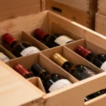 Wine bottles organised in a wooden storage box as part of a growing wine collection.